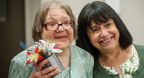 Woman with developmental disability holds a handmade centerpiece and smiles with a member of her staff.