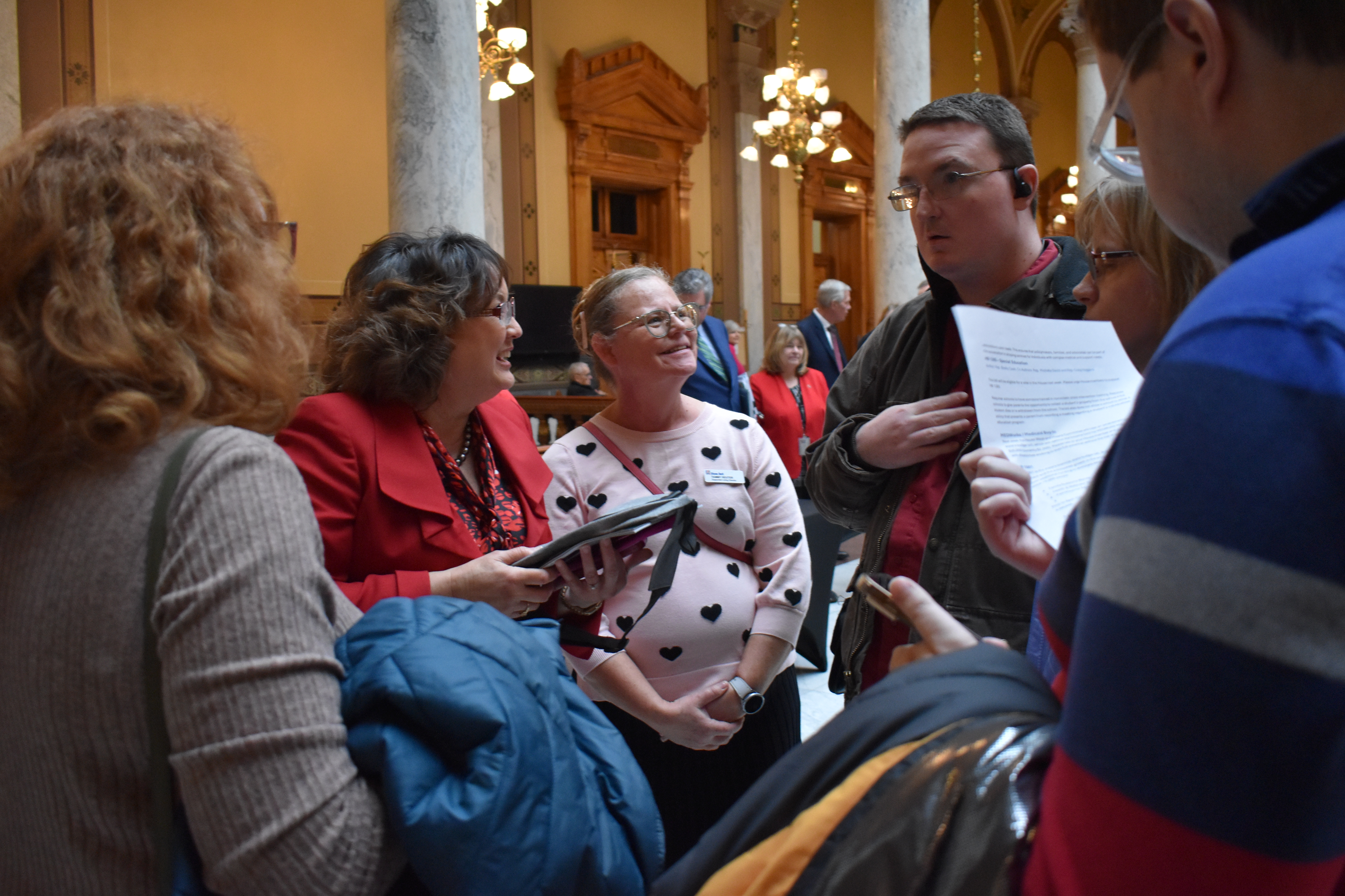 A young man using a wheelchair and communication device talks with a female legislator as his peers watch.